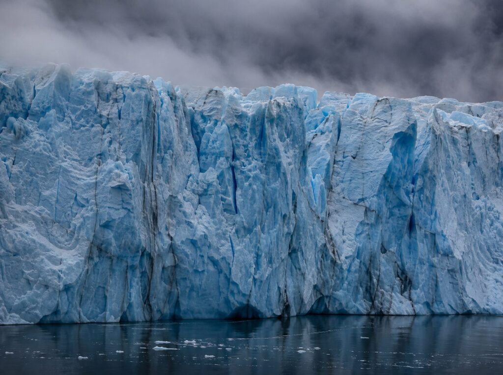 The face of a glacier meeting dark still water under low cloud
