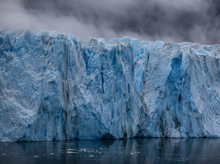 The face of a glacier meeting dark still water under low cloud